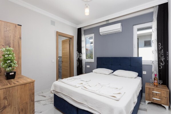Een slaapkamer met een bed, een houten nachtkastje, een potplant en een airconditioning.