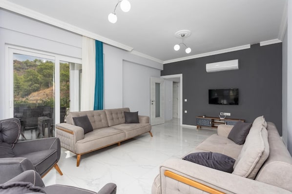 Een moderne woonkamer met een bank, fauteuils en een televisie.