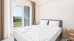 Ein Hotelzimmer mit Bett, Nachttisch, Vorhängen und Blick ins Freie.