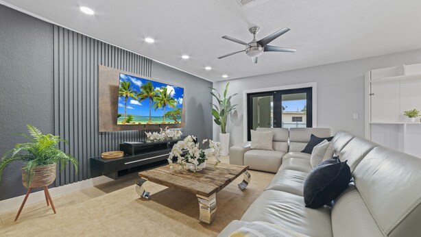 A modern living room with a sofa, coffee table, TV, and ceiling fan. - Retreat Near Hard Rock • Pool, BBQ & Game Room (Miami Gardens)