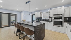 A modern kitchen with white cabinets, a black marble island, and a stainless steel oven. - Retreat Near Hard Rock • Pool, BBQ & Game Room (Miami Gardens)