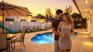 A couple standing by a swimming pool with lounge chairs and a slide in the background. - Retreat Near Hard Rock • Pool, BBQ & Game Room (Miami Gardens)