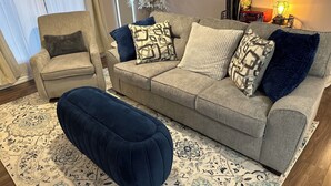 A living room with a grey sofa, a blue ottoman, and a patterned rug. - Round Rock Supernova minutes from Kalahari, Round Rock Sports Complex, and DT  (Round Rock)