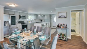 A modern kitchen with stainless steel appliances, a dining area with a glass table, and a bar cart with bottles. - Weymouth Waterfront Getaway w/ Swim Spa & Hot Tub (Weymouth)