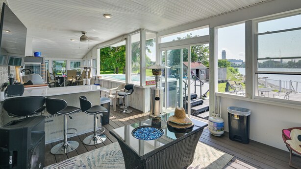 A spacious indoor area with a large window overlooking a body of water, a bar area with stools, and a seating area with a glass-top table. - Weymouth Waterfront Getaway w/ Swim Spa & Hot Tub (Weymouth)