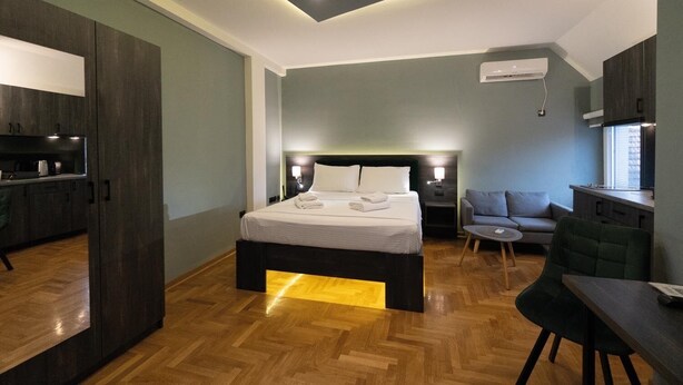 A modern hotel room with a large bed, a desk, a sofa, and a kitchenette. - Aleksei apartments (Belgrade)