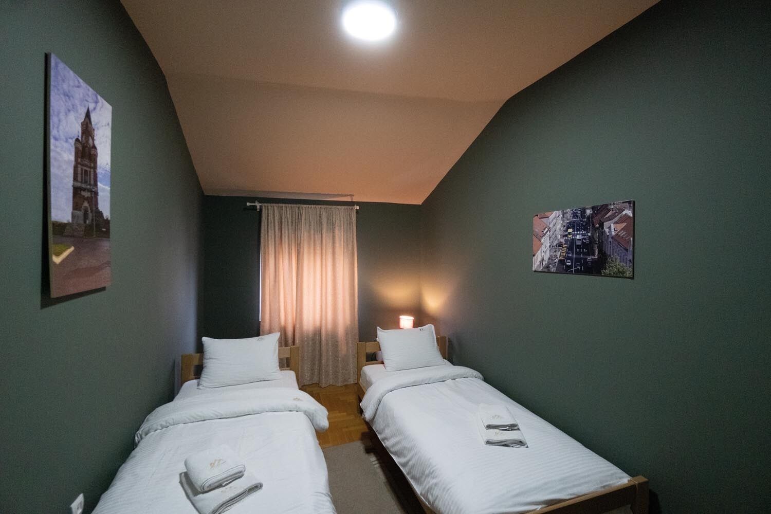 A room with two single beds, a curtain, and two wall-mounted pictures.