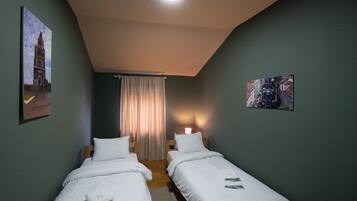 A room with two single beds, a curtain, and two wall-mounted pictures.