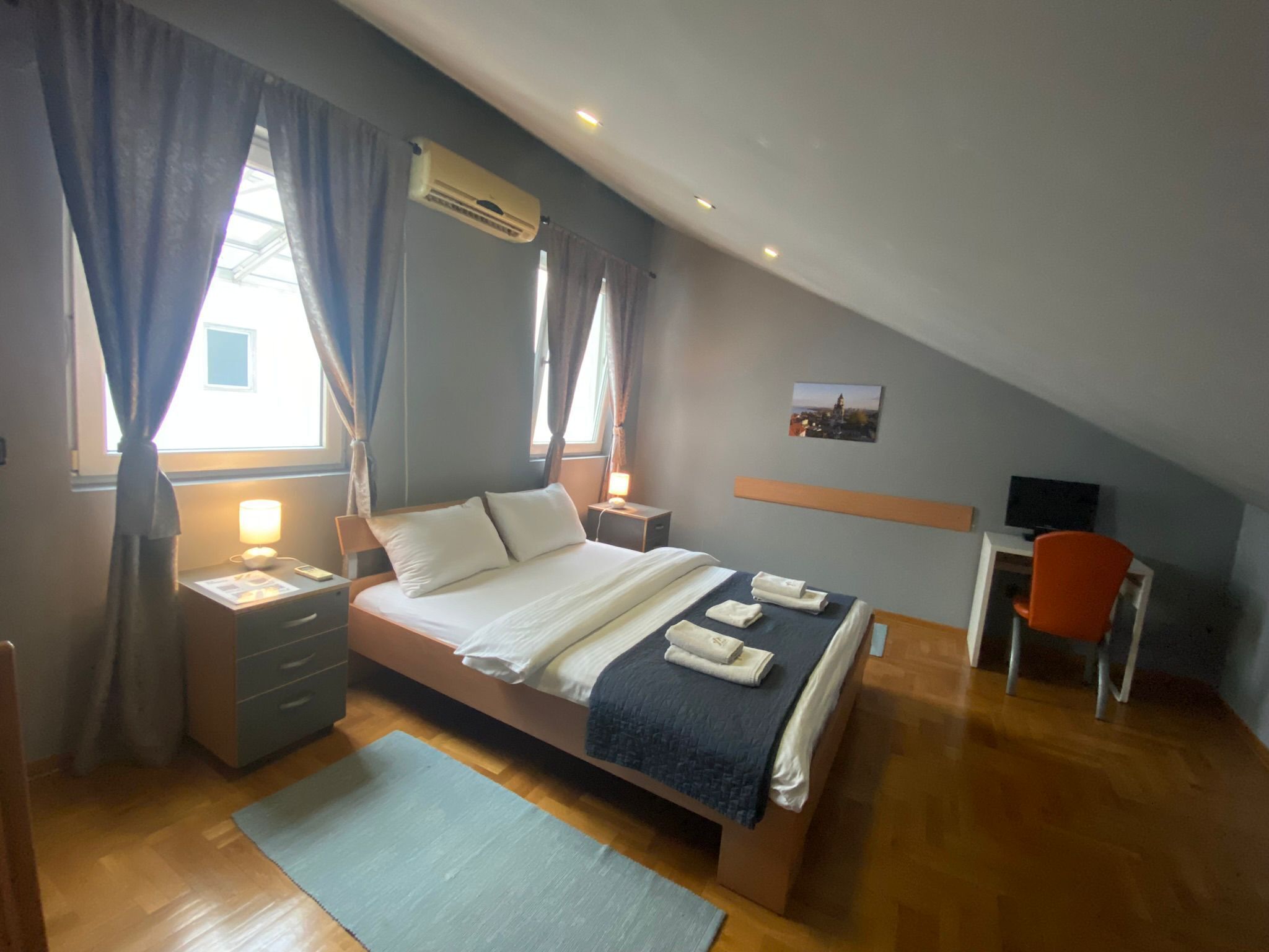 A bedroom with a bed, bedside tables, a desk, and an air conditioner.