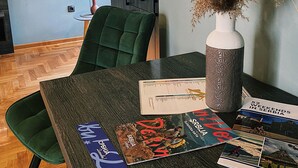 A dining area with a dark wooden table, green upholstered chairs, and a vase with dried plants. - Aleksei apartments (Belgrade)