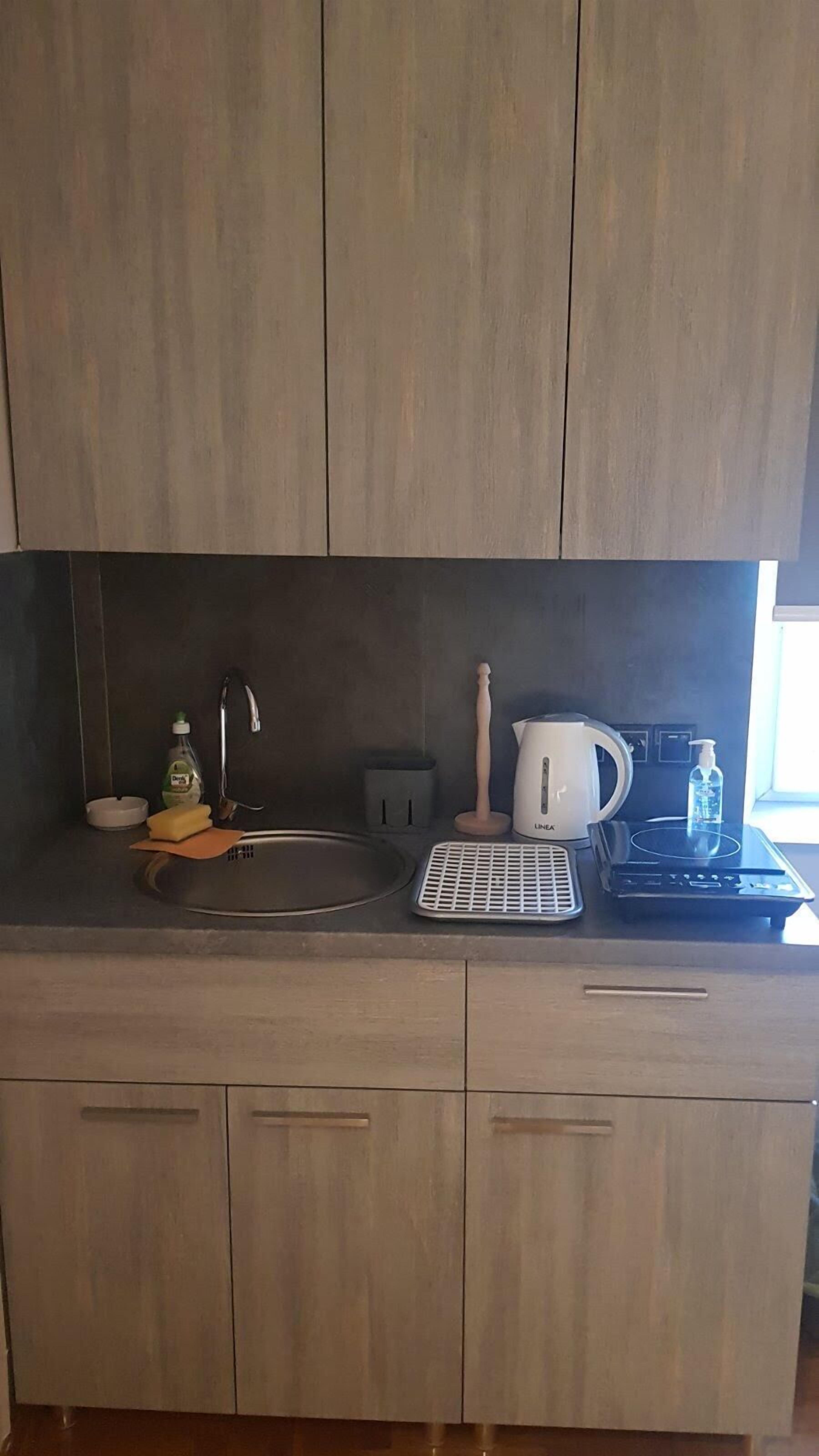 Et moderne køkken med træskabe, en vask, elkedel, kaffemaskine og en flaske opvaskemiddel.