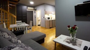 A modern living room with a gray sofa, a dining table with chairs, a kitchen area, and a staircase. - Aleksei apartments (Belgrade)