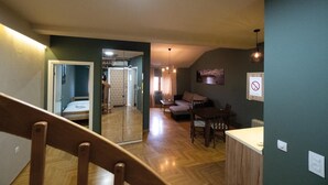 A spacious living area with a wooden floor, a sofa, a dining table, and a staircase leading to another room. - Aleksei apartments (Belgrade)