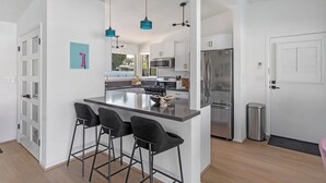 A modern kitchen with a central island, bar stools, and stainless steel appliances. - Poolside at Panorama - Walk to El Paseo (Palm Desert)