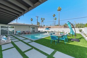 A modern outdoor pool area with a patio, seating, and palm trees in the background. - Poolside at Panorama - Walk to El Paseo (Palm Desert)