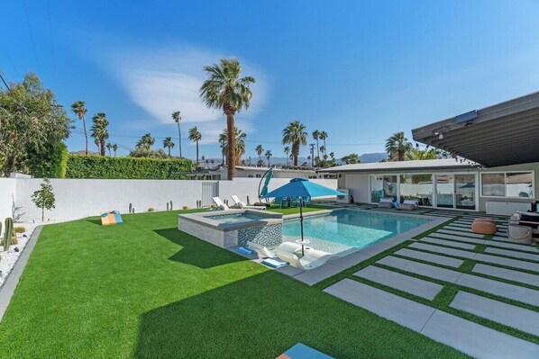 A modern outdoor pool area with a rectangular pool, lounge chairs, and a blue umbrella. - Poolside at Panorama - Walk to El Paseo (Palm Desert)