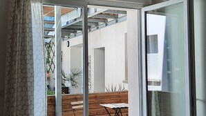 Ein modernes Interieur mit einem Holzespeisetisch und -stühlen, einem gemusterten Vorhang und Blick auf einen Außenbereich mit Holzdeck und Blumentöpfen.