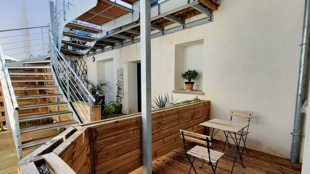 Eine Holzterrasse mit integriertem Bank und Tisch, eine Treppe mit Metallgeländern und ein Blumentopf an der Wand.