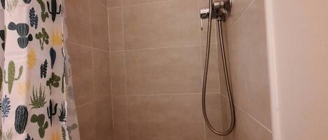 A shower area with a showerhead and hose, a drain, and a shower curtain with a cactus pattern.