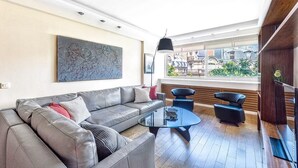 Una sala de estar moderna con un sofá gris, una mesa de centro de vidrio y vistas de edificios a través de amplios ventanales.