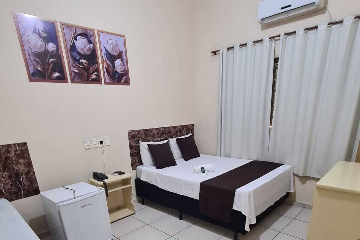 A hotel room with a bed, a desk, a chair, and a small refrigerator.
