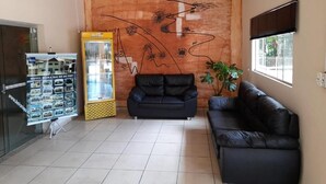 Un hall de hotel con un gran mural abstracto, un sofá de cuero negro, un refrigerador y una exhibición de folletos del hotel.