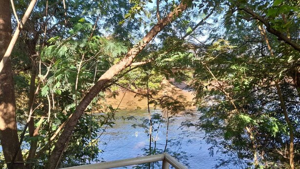 Una terraza de madera con vistas a un río tranquilo y un denso follaje al fondo.