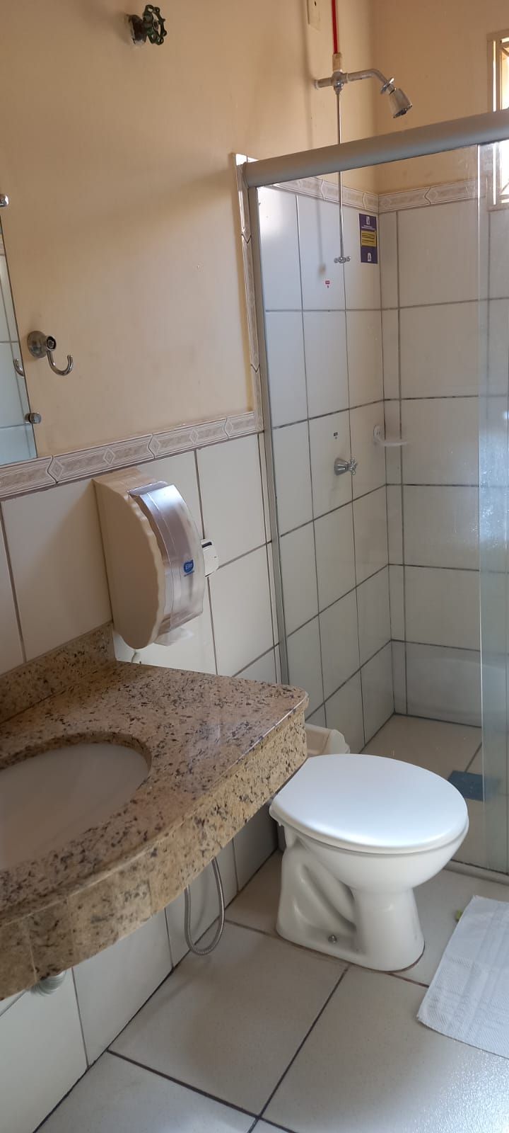 A bathroom with a toilet, a sink with a paper towel dispenser, and a shower area.
