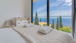 A bedroom with a large window, a bed with white linens, a bedside lamp, and a view of the sea. - CR7 Airport View (Santa Cruz)