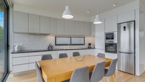 A modern kitchen with white cabinets, a stainless steel refrigerator, and a wooden dining table with chairs. - CR7 Airport View (Santa Cruz)