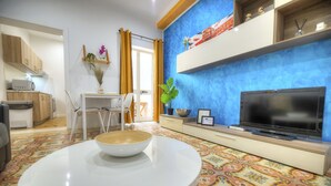 A modern living room with a round white table, a flat-screen TV, and a patterned carpet. - Charming 2 bedroom townhouse, internal yard JDES1-1 (Gzira)