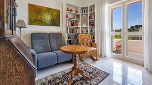 A living room with a sofa, a round wooden table, a bookshelf, and a large window.