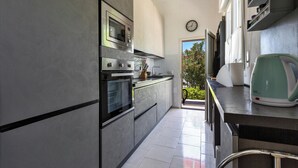 A modern kitchen with stainless steel appliances, a clock on the wall, and a view of greenery outside.