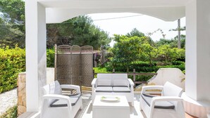 An outdoor patio with white wicker furniture, including a sofa and chairs, and a small table with a plate.