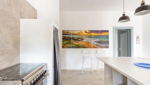 A modern kitchen with a stove, white chairs, and a large painting on the wall.