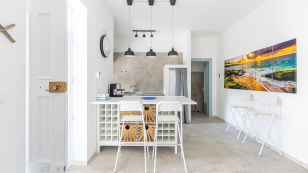 A modern kitchen with white cabinetry, a central island with stools, pendant lighting, and a large landscape painting on the wall.