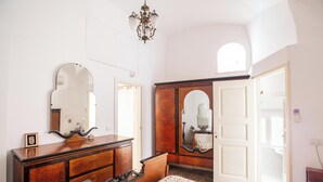 Um quarto com cômoda de madeira, cama com colcha estampada, espelho grande e janela em arco.