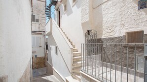 Um beco estreito com uma escadaria que leva a um edifício, com guarda-corpo de metal e parede de pedra.
