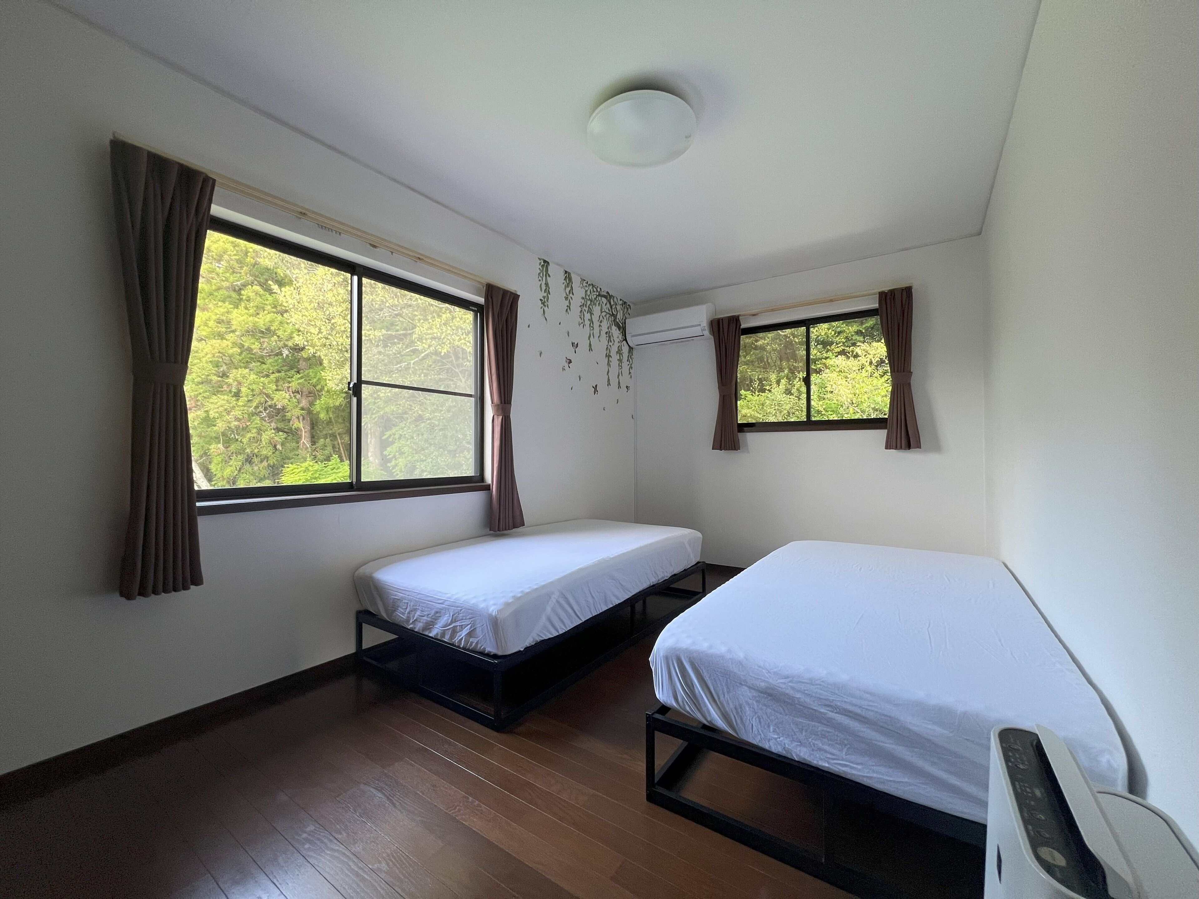 Un alojamiento pequeño de una sola habitación con dos camas individuales, una ventana con cortinas y una lámpara en el techo.