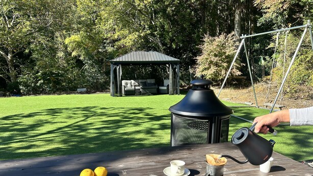 Una mesa de madera con tazas, limones y una tetera en un jardín con un pabellón y árboles.