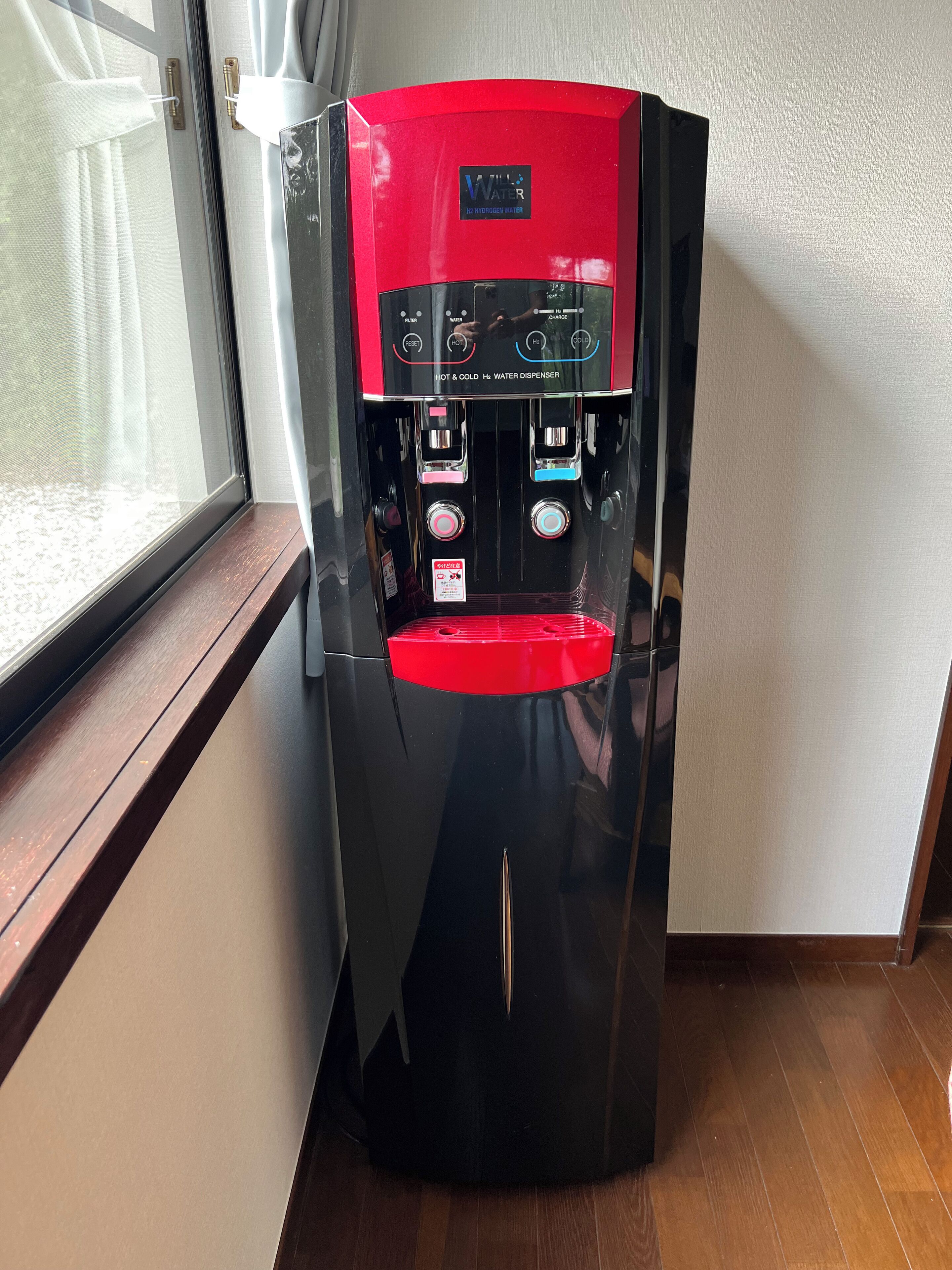 En kompakt, svart vattenautomat med ett rött lock, som erbjuder både varmt och kallt vatten samt ett alternativ för väteberikat vatten.