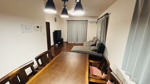 Un comedor con una larga mesa de madera, varias sillas, un televisor y un sofá al fondo.