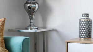 Ein modernes Wohnzimmer mit einem Glastisch, einem türkisfarbenen Sofa, einer schwarzen Lampe und einer dekorativen Vase.