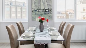 Ein Esszimmer mit gedecktem Tisch für vier Personen, einer Blumenvase und einem Gemälde eines Segelboots an der Wand.