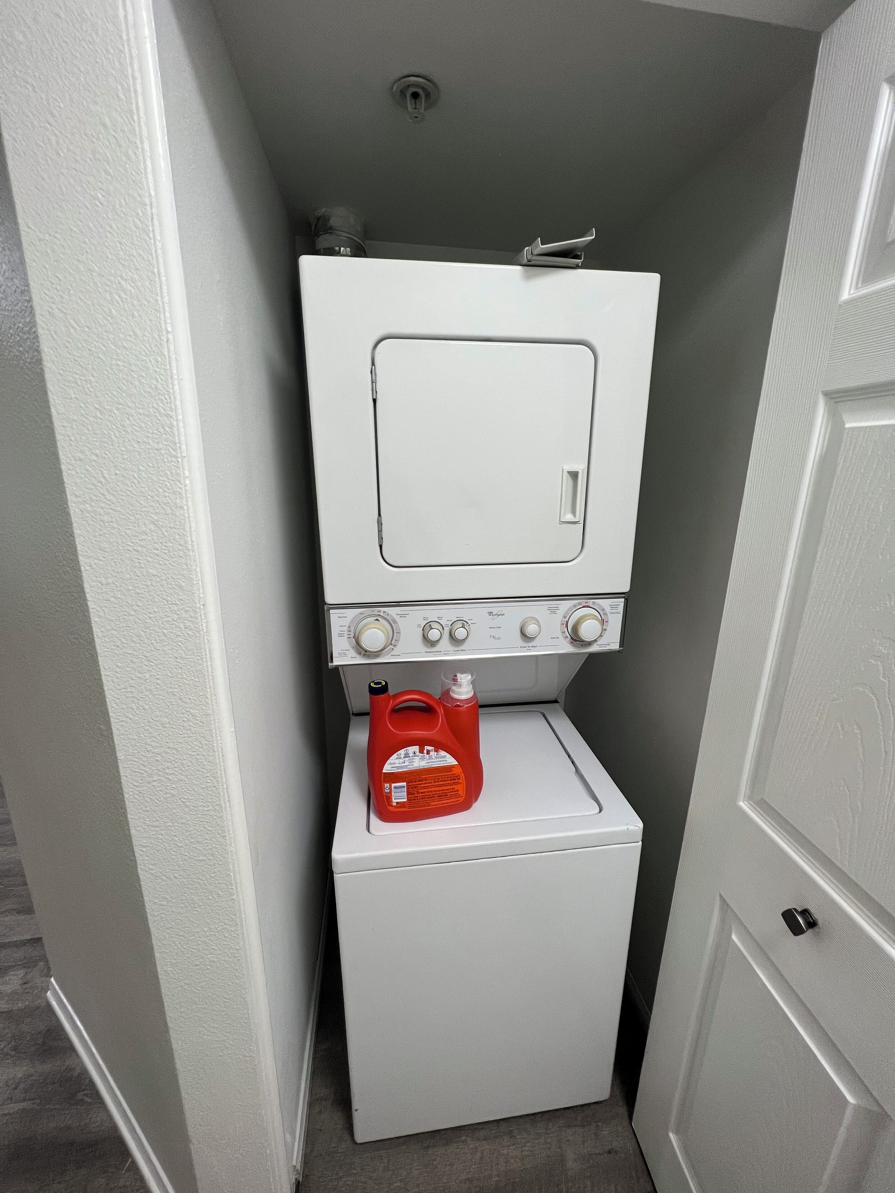 A compact laundry room with a washing machine and a dryer, a small cabinet above the dryer, and a red detergent bottle on the machine.