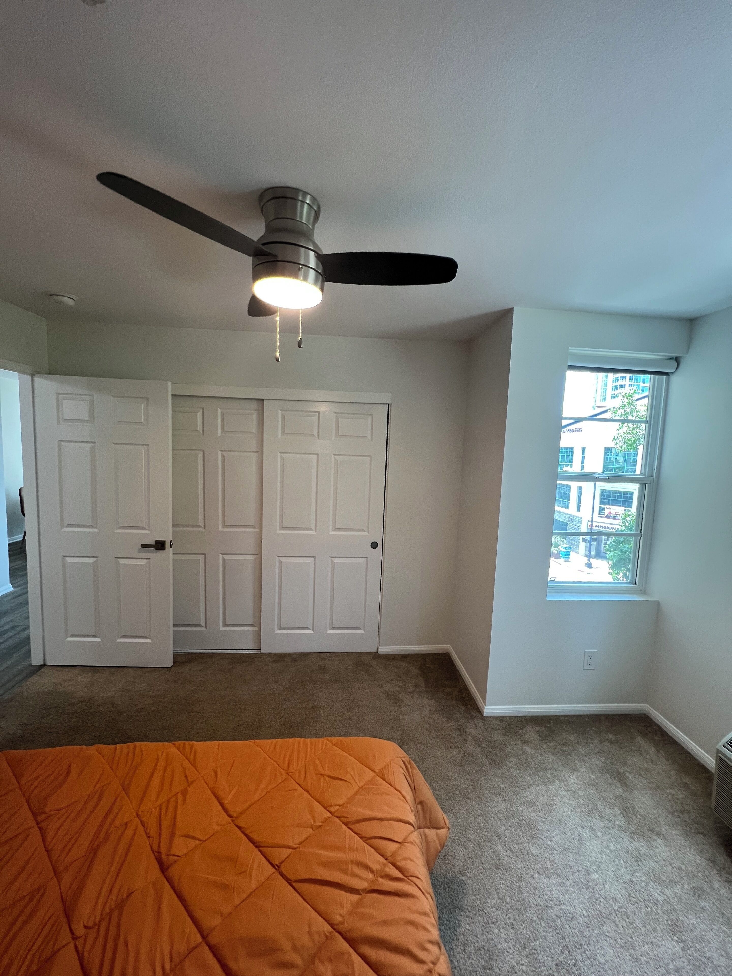 A bedroom with a bed, a ceiling fan, a window, and a door.
