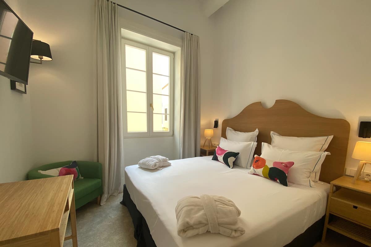 Una habitación de hotel con cama, escritorio, silla y ventana con cortinas.
