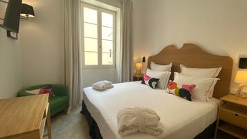 Una habitación de hotel con cama, escritorio, silla y ventana con cortinas.