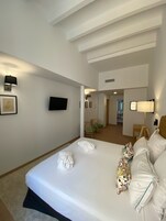 Una habitación de hotel con una cama grande, un televisor de pantalla plana montado en la pared, un escritorio con una lámpara y una silla con un cojín verde.