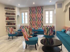 Una sala moderna con sofás color turquesa, sillones a rayas y una estantería llena de libros.